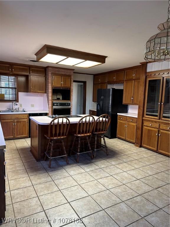 kitchen with a breakfast bar, black fridge, decorative light fixtures, a kitchen island, and wall oven