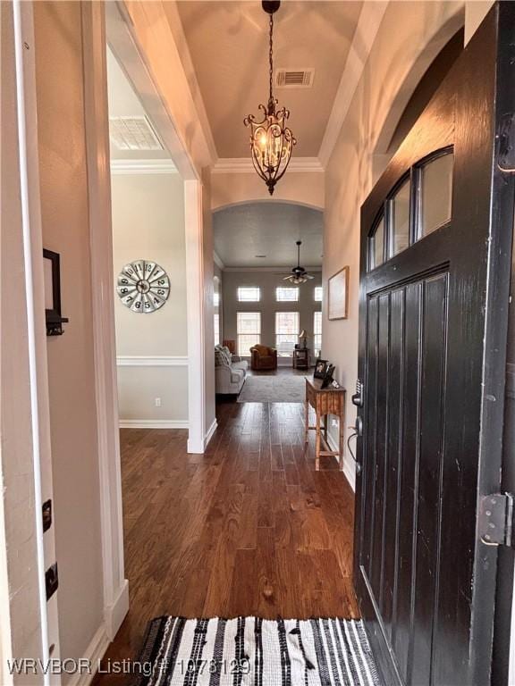 foyer entrance with ceiling fan with notable chandelier, ornamental molding, and dark wood-type flooring