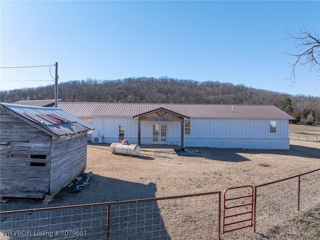 view of front facade featuring board and batten siding, fence, french doors, metal roof, and crawl space