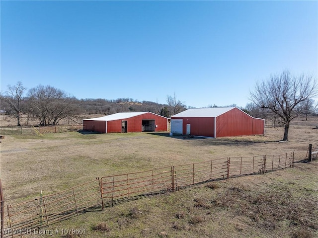 view of yard with a rural view, a detached garage, fence, and a pole building