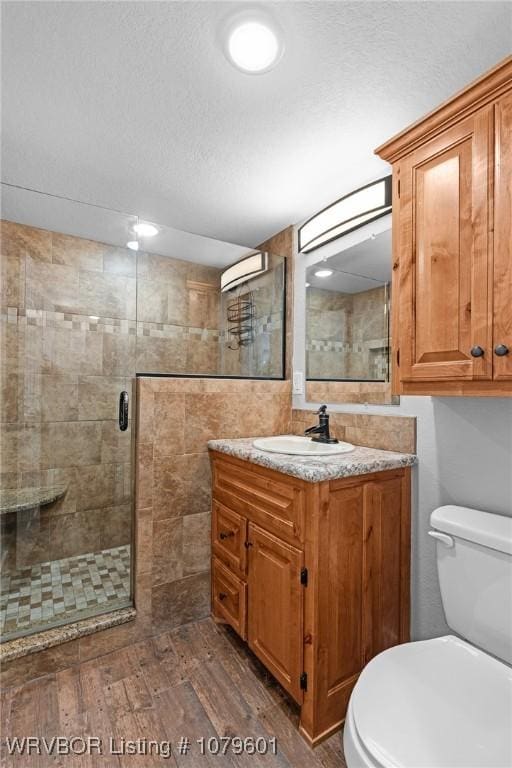 full bathroom featuring toilet, a textured ceiling, wood finished floors, a shower stall, and vanity