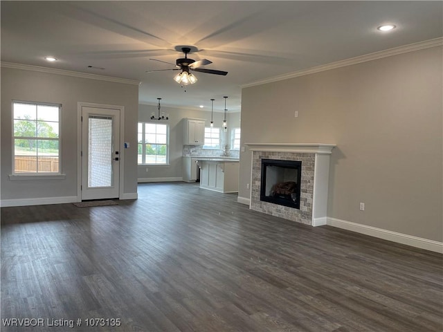 unfurnished living room featuring dark hardwood / wood-style floors, crown molding, ceiling fan with notable chandelier, and a tile fireplace