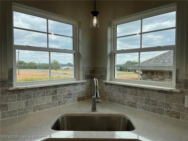 details featuring pendant lighting, decorative backsplash, light stone counters, and sink