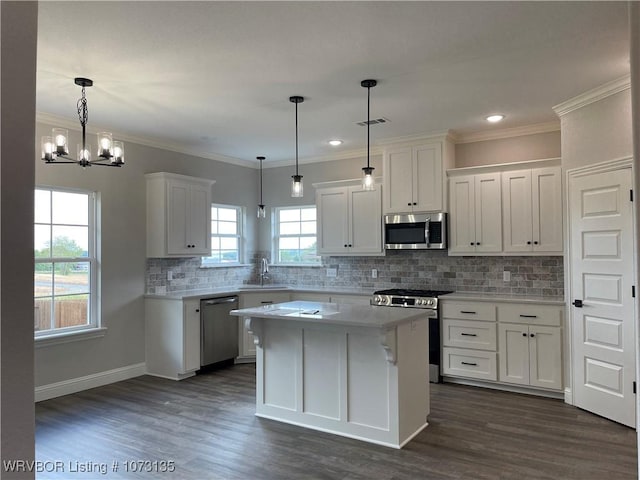 kitchen featuring stainless steel appliances, sink, pendant lighting, white cabinets, and a center island