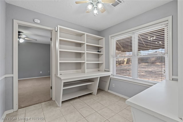 interior space with a textured ceiling, light tile patterned flooring, visible vents, baseboards, and a ceiling fan