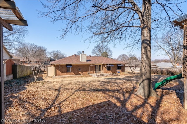 rear view of house featuring brick siding, a chimney, a playground, and fence