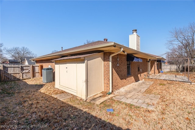 exterior space with central AC, brick siding, fence, and a chimney