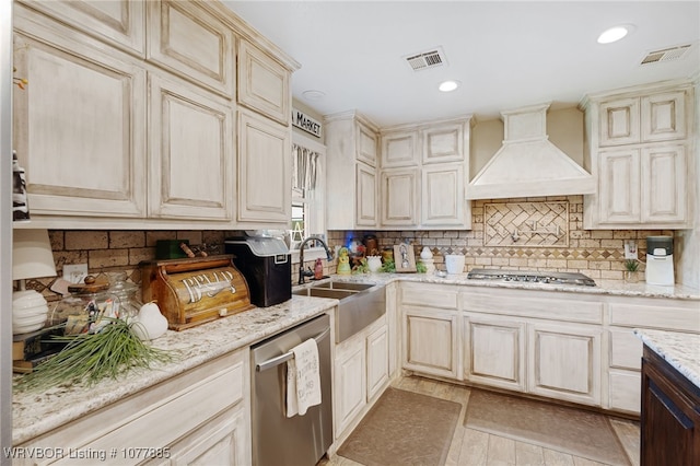 kitchen with light stone countertops, sink, stainless steel appliances, cream cabinetry, and custom exhaust hood