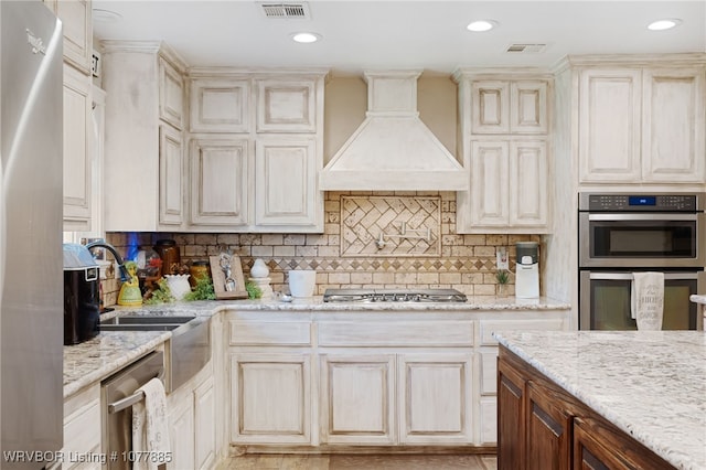 kitchen featuring light stone countertops, tasteful backsplash, custom exhaust hood, stainless steel appliances, and sink