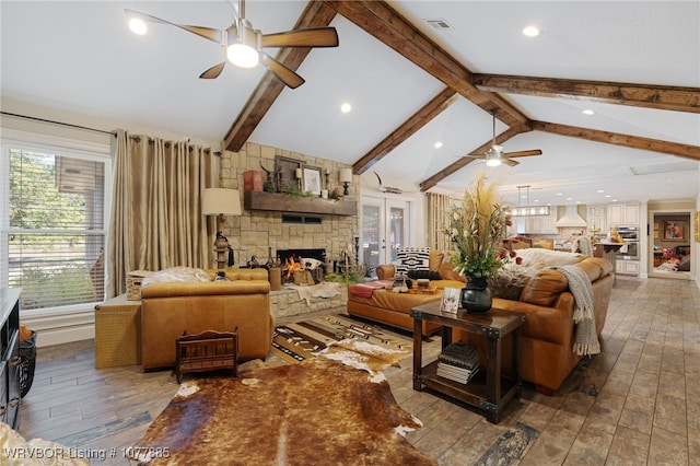 living room featuring hardwood / wood-style floors, high vaulted ceiling, a stone fireplace, ceiling fan, and beamed ceiling