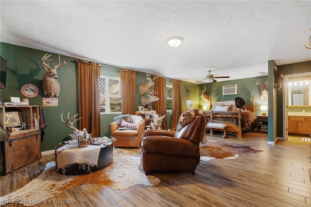 bedroom featuring hardwood / wood-style flooring, ceiling fan, a textured ceiling, connected bathroom, and a wall unit AC