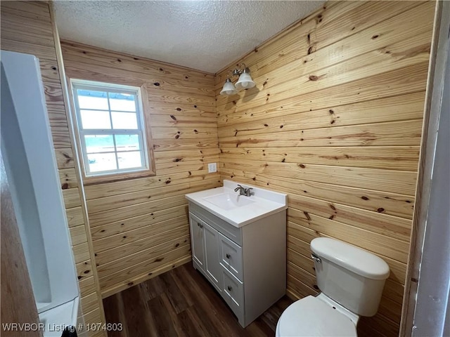 bathroom with vanity, wooden walls, hardwood / wood-style flooring, toilet, and a textured ceiling