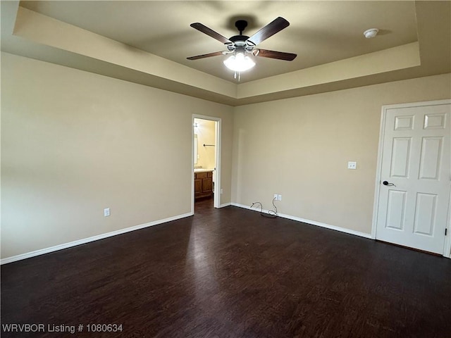 spare room featuring baseboards, a raised ceiling, ceiling fan, and dark wood-style flooring