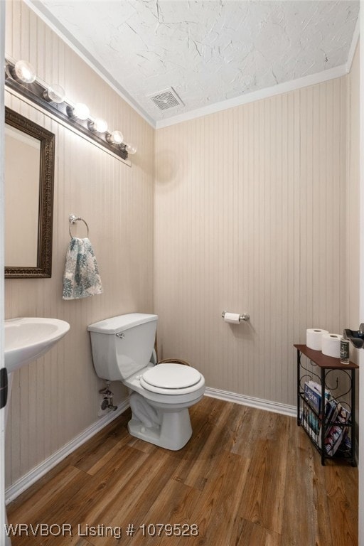 bathroom with toilet, wood finished floors, visible vents, and ornamental molding