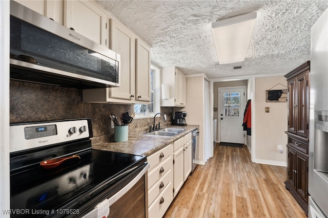 kitchen with light wood finished floors, decorative backsplash, appliances with stainless steel finishes, a textured ceiling, and a sink