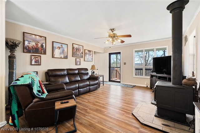 living room with wood finished floors, crown molding, baseboards, ceiling fan, and a wood stove