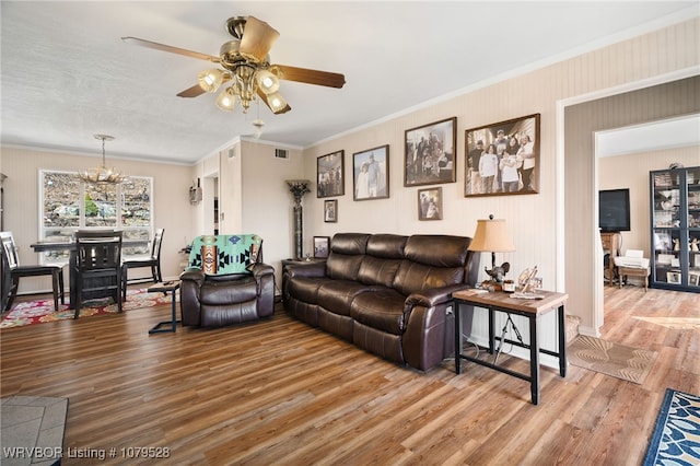 living area featuring crown molding, light wood-style flooring, ceiling fan with notable chandelier, and visible vents