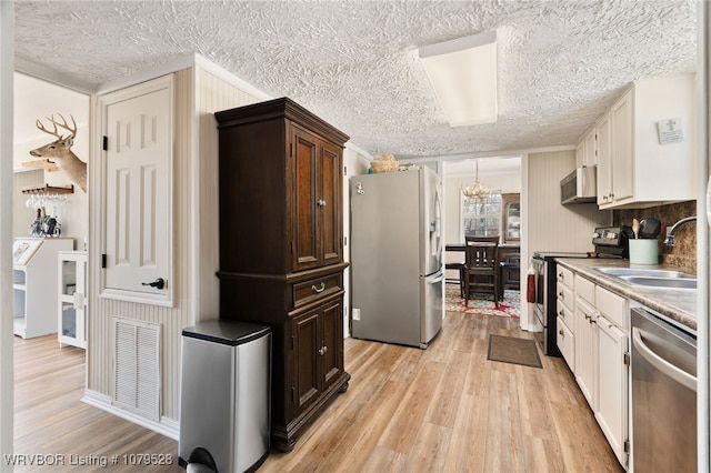 kitchen with visible vents, light wood-style flooring, a sink, stainless steel appliances, and a chandelier