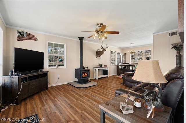 living room featuring visible vents, ornamental molding, ceiling fan with notable chandelier, a wood stove, and wood finished floors