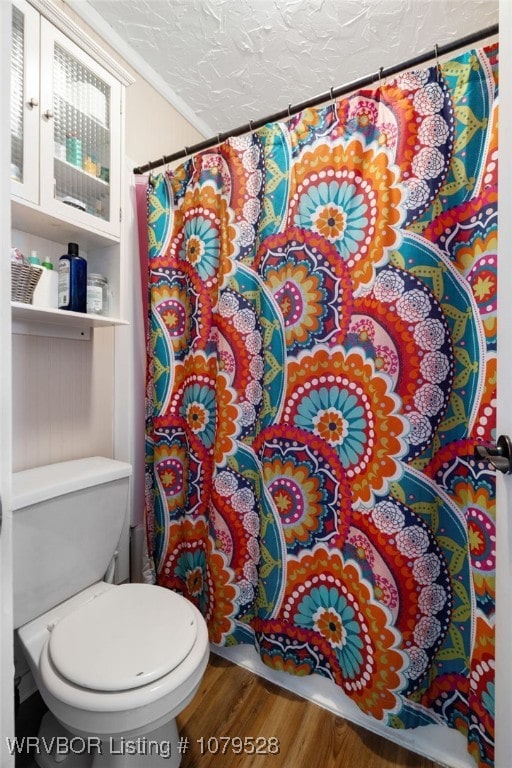 bathroom with toilet, a textured ceiling, a shower with curtain, and wood finished floors