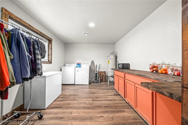 clothes washing area with cabinets, electric water heater, independent washer and dryer, wood-type flooring, and a textured ceiling