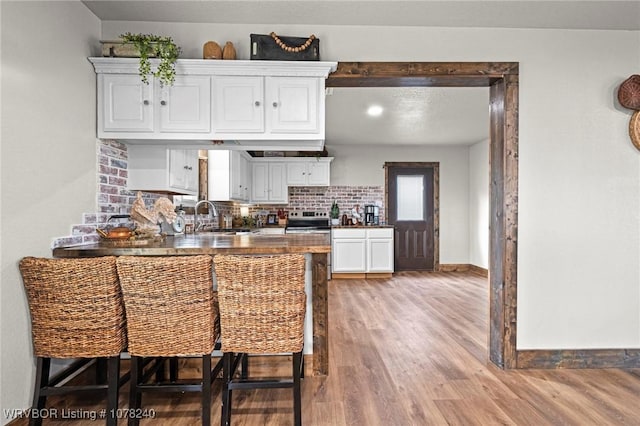 kitchen featuring decorative backsplash, stainless steel range with electric stovetop, sink, hardwood / wood-style floors, and white cabinetry