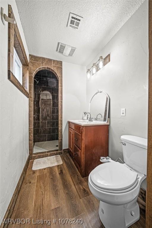 bathroom with a textured ceiling, tiled shower, toilet, vanity, and hardwood / wood-style flooring