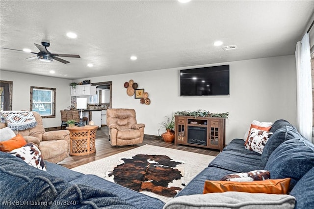 living room with hardwood / wood-style flooring, ceiling fan, and a textured ceiling