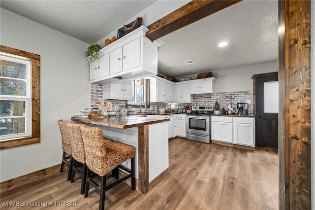 kitchen with stainless steel electric stove, white cabinets, sink, kitchen peninsula, and a breakfast bar area