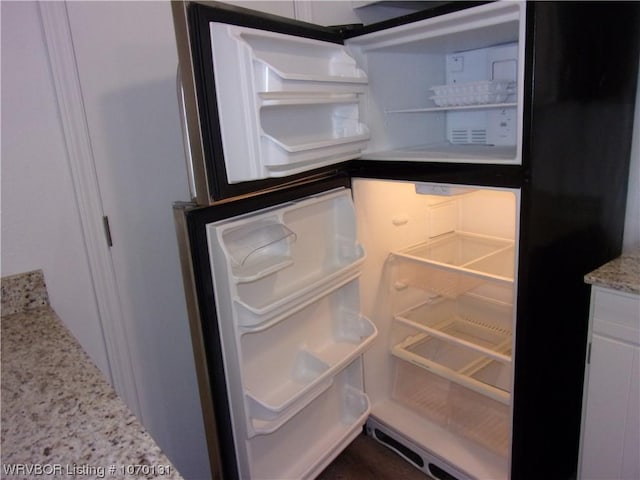 room details with white cabinets, refrigerator, and light stone counters