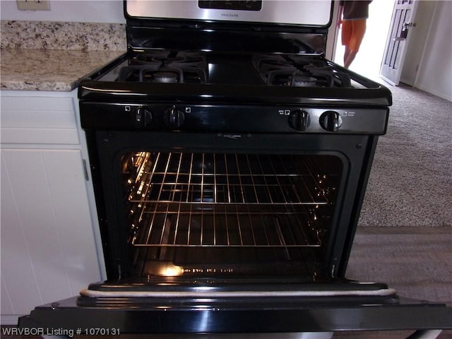 interior details with black gas range, white cabinets, and carpet