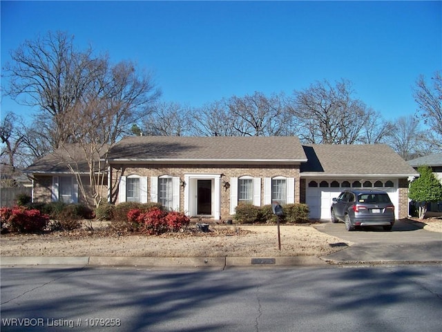 single story home featuring driveway, an attached garage, a shingled roof, and brick siding