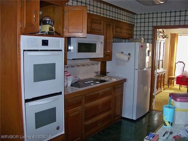 kitchen featuring white appliances, wallpapered walls, dark tile patterned flooring, brown cabinets, and light countertops