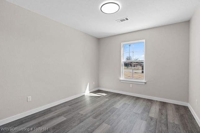 spare room with dark wood finished floors, visible vents, and baseboards