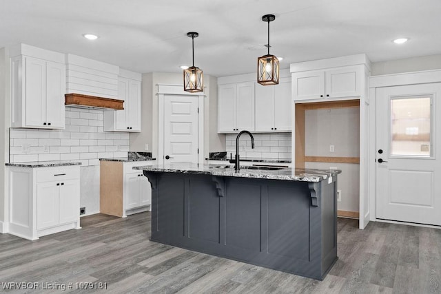 kitchen with a kitchen island with sink, pendant lighting, white cabinetry, and dark stone countertops