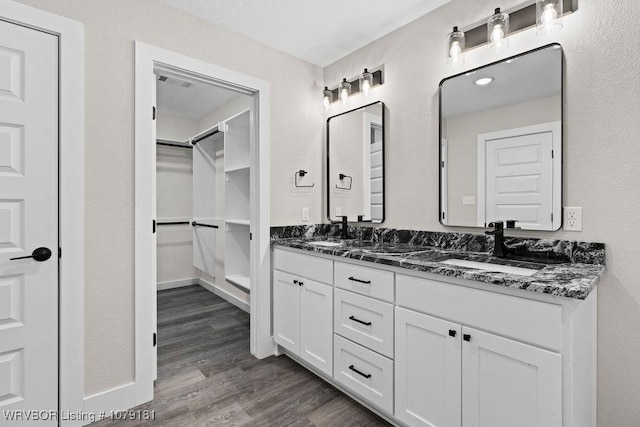 bathroom with double vanity, visible vents, wood finished floors, a spacious closet, and a sink