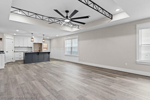 unfurnished living room with a skylight, light wood finished floors, recessed lighting, a ceiling fan, and baseboards