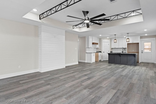 unfurnished living room featuring ceiling fan, a sink, wood finished floors, and baseboards