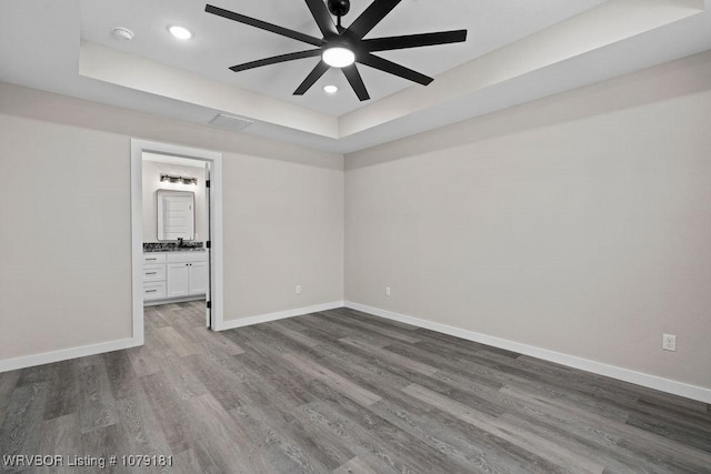 unfurnished bedroom featuring recessed lighting, wood finished floors, visible vents, baseboards, and a raised ceiling