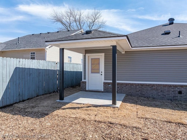 property entrance featuring a shingled roof, a patio area, fence, and brick siding