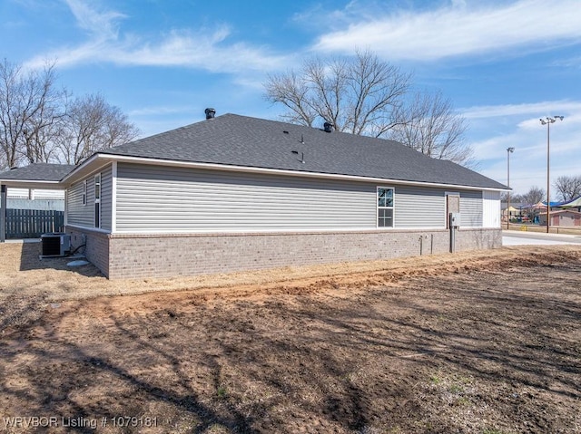 view of home's exterior with brick siding, roof with shingles, and central air condition unit