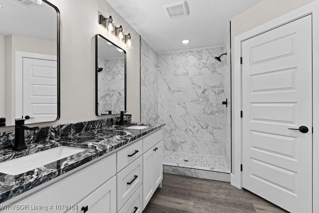 bathroom with double vanity, a sink, a tile shower, and wood finished floors