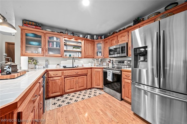 106078 S 4715th Rd, Muldrow, OK 74948 - kitchen featuring stainless steel appliances, tile countertops, light wood-style floors, glass insert cabinets, and brown cabinets