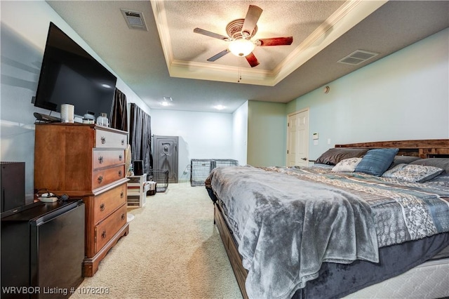 bedroom with a textured ceiling, a tray ceiling, light colored carpet, ceiling fan, and crown molding