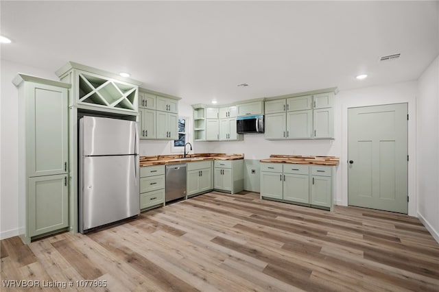 kitchen with green cabinets, butcher block counters, sink, and appliances with stainless steel finishes