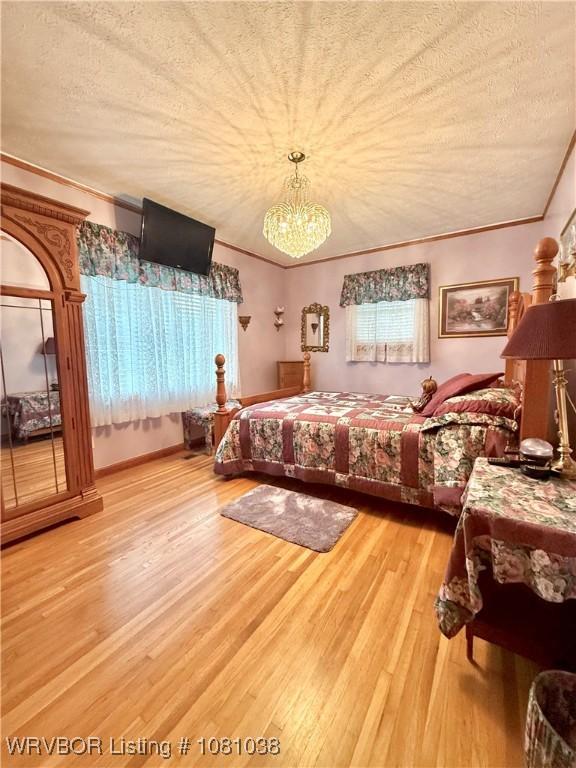bedroom featuring wood finished floors, crown molding, a textured ceiling, a chandelier, and multiple windows