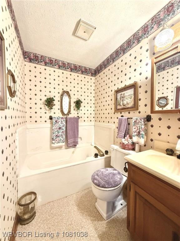 full bathroom with wallpapered walls, a garden tub, a textured ceiling, toilet, and vanity