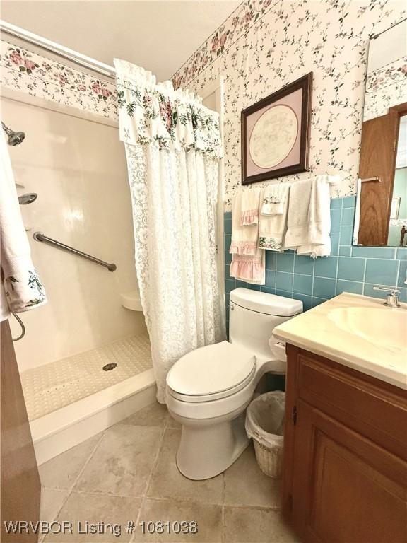 full bathroom with wallpapered walls, a stall shower, toilet, vanity, and tile patterned floors
