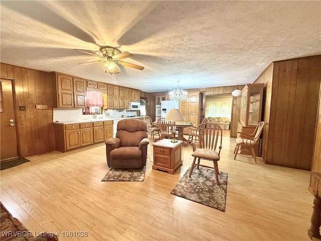 living room featuring wood walls, a textured ceiling, a chandelier, a ceiling fan, and light wood finished floors