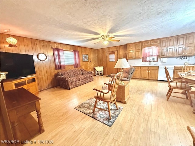 living room with ceiling fan, a textured ceiling, light wood-type flooring, and wood walls